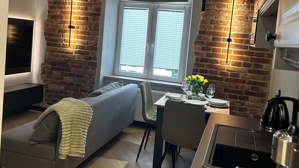 A modern kitchen with a brick wall, a dining area with a sofa, and a TV mounted on the wall. - Charm & Comfort Renovated Gem in Old Town 8 min walk to Krakow’s Main Square!  (Kraków)