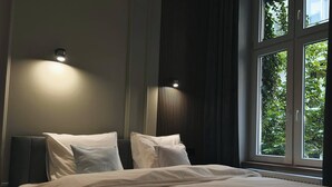 A bedroom with a large bed, two bedside tables, a wall-mounted light, and a window with a view of greenery. - Charm & Comfort Renovated Gem in Old Town 8 min walk to Krakow’s Main Square!  (Kraków)