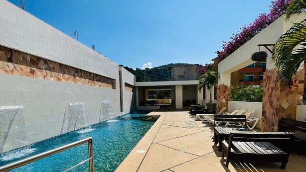 A poolside area with a clear blue pool, lounge chairs, and a stone wall. - Amparo Resort (Los Ayala)