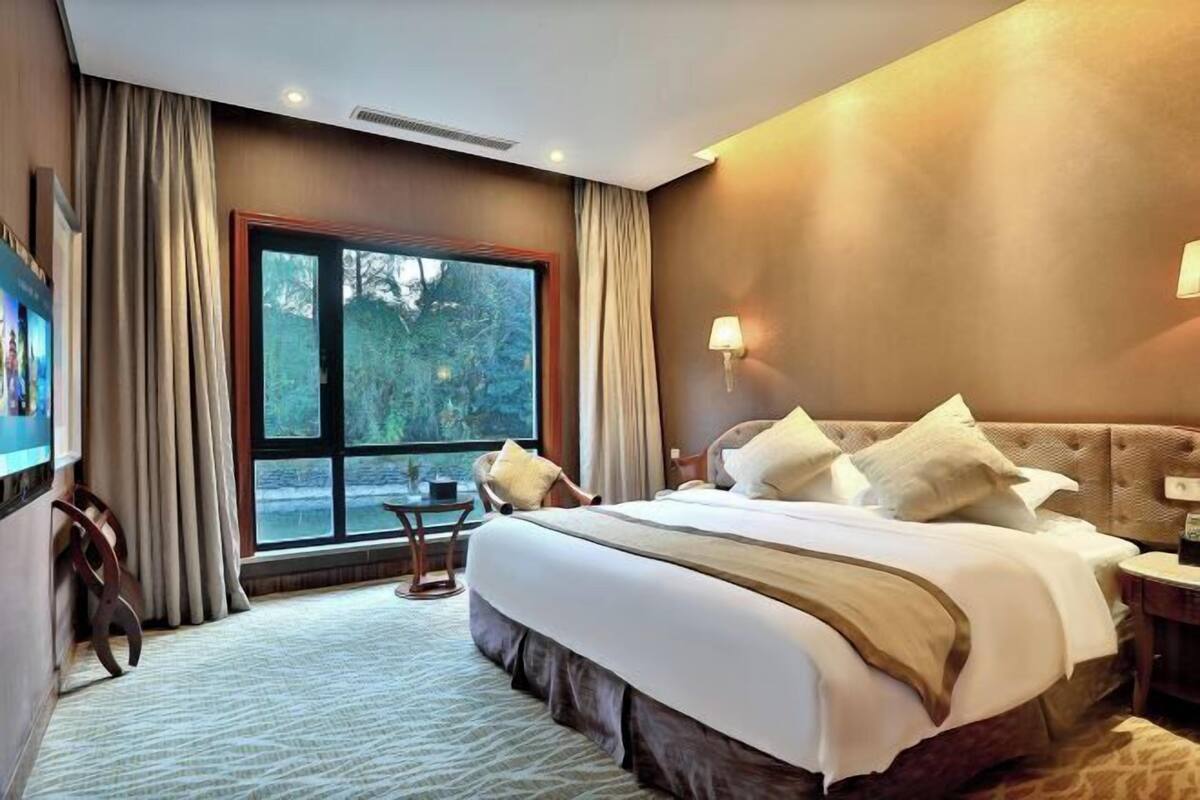 Habitació d'hotel amb un llit gran, una finestra amb cortines, una làmpada penjada a la paret i una televisió.