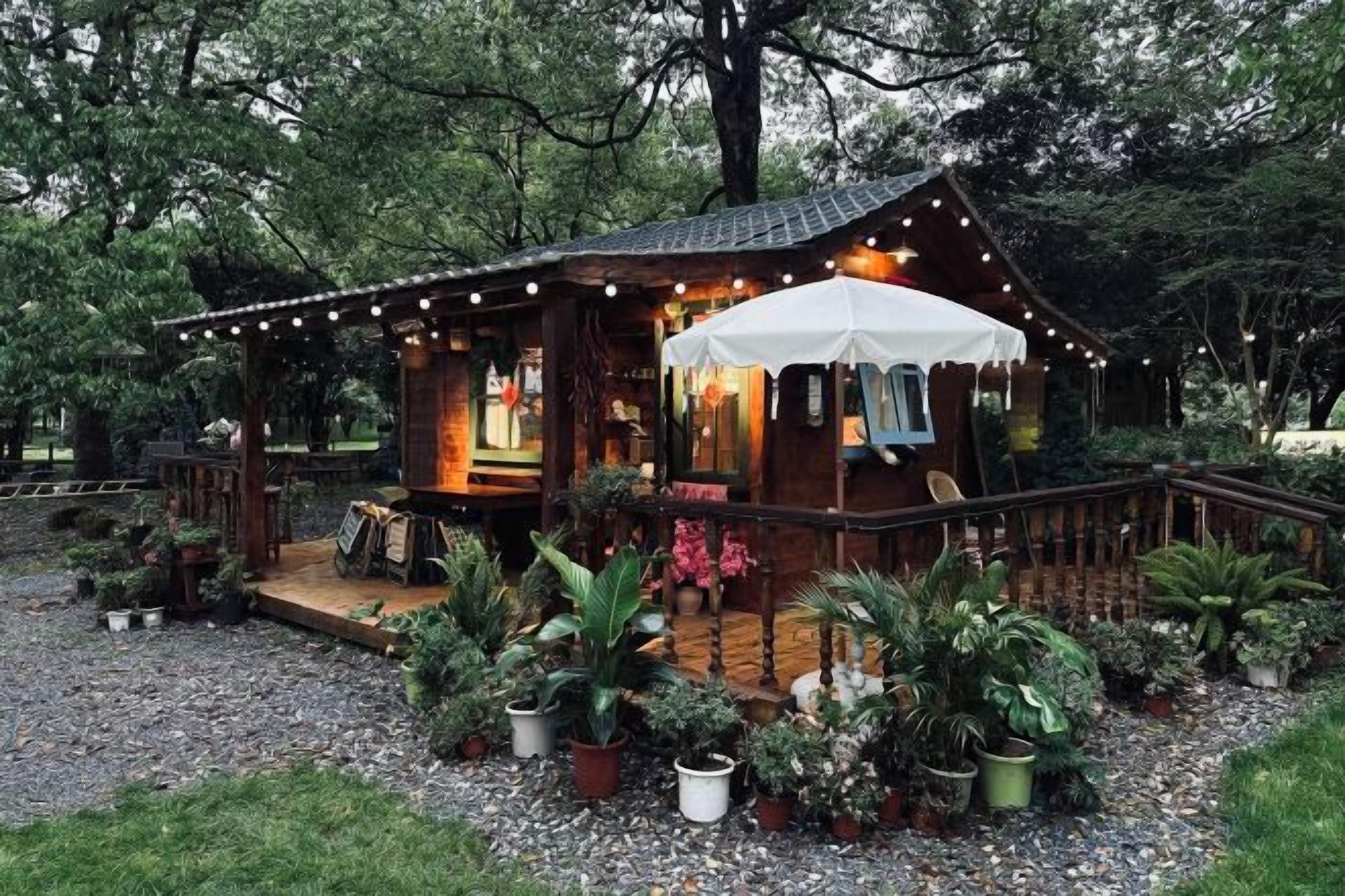 Une cabane en bois dotée d’un porche, entourée de plantes en pot et bordée d’un chemin de gravier.