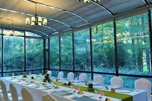 A long table set for a meal with chairs, a chandelier, and large windows with a forest view. - Weisheng Xiangyi Hotel (Xiangyi Building) (Anji)