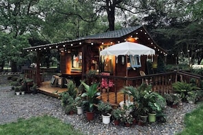 A wooden cabin with a porch, surrounded by potted plants and a gravel path. - Weisheng Xiangyi Hotel (Xiangyi Building) (Anji)