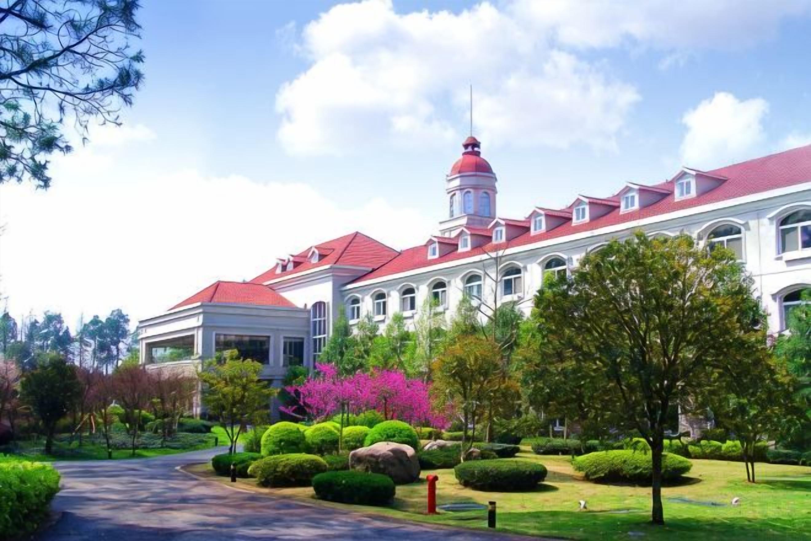 A large building with a red roof and a tower, surrounded by well-maintained gardens and a pathway.