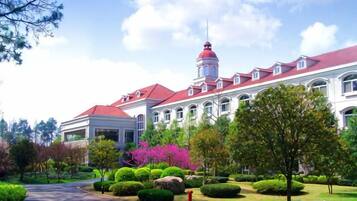 A large building with a red roof and a tower, surrounded by well-maintained gardens and a pathway.