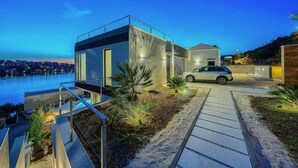 Ein modernes Haus mit einem geparkten Auto voran, einem Weg zum Eingang und Blick auf Wasser und Stadt im Hintergrund.