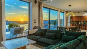 Ein modernes Wohnzimmer mit einer großen Couch, einem Couchtisch und Blick auf einen Sonnenuntergang über dem Wasser.