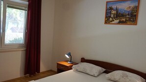 Ein Schlafzimmer mit einem Bett, einem Nachttisch mit Lampe, einem Fenster mit Vorhängen und einem Bild an der Wand.