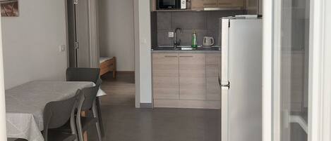 Een kleine keuken met een magnetron, waterkoker en een koelkast. Er is een eethoek met een tafel en stoelen.