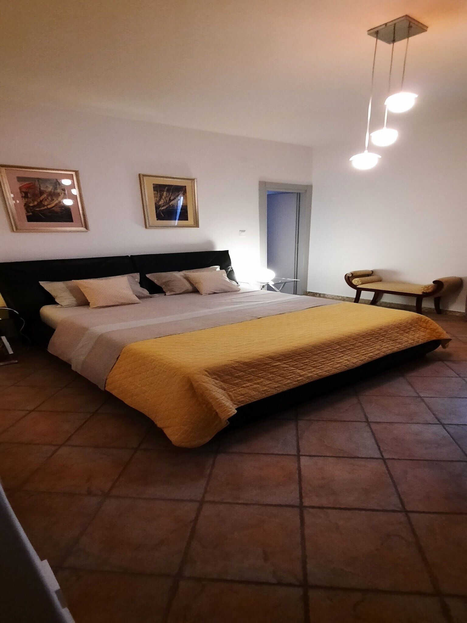 A bedroom with a large bed, a chair, and two framed pictures on the wall.
