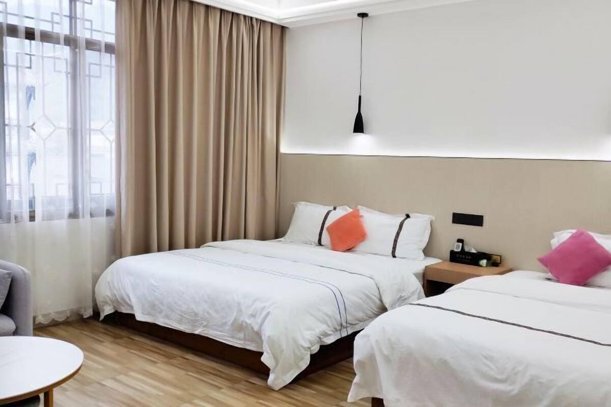 A hotel room with two beds, a desk, a chair, a nightstand, and a window with curtains.