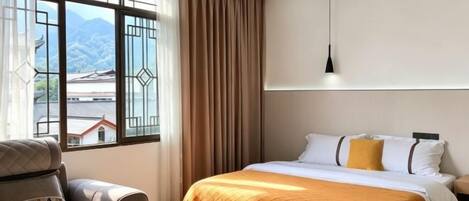 A hotel room with a bed, a chair, a table, and a window with curtains.