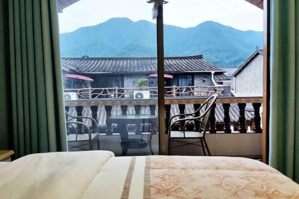 Ein Zimmer mit einem Bett, einem Balkon mit Tisch und Stühlen sowie Blick auf traditionelle Gebäude und Berge.