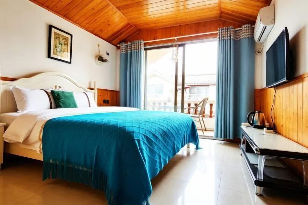 A hotel room with a bed, a desk, a TV, and a balcony with curtains.
