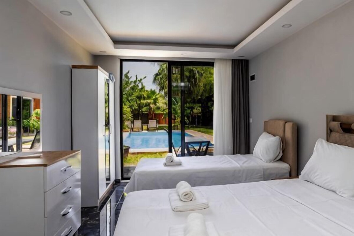 Quarto de hotel com duas camas, uma mesa, uma cadeira e vista para uma piscina.