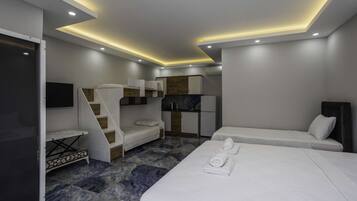 Una habitación de hotel moderna con una cama grande, una cama más pequeña, una zona de estar, una kitchenette y un televisor.