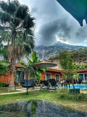 A pool area with lounge chairs and a hanging chair, surrounded by palm trees and a mountain backdrop. - Terra Garden Hotel  (Kemer)
