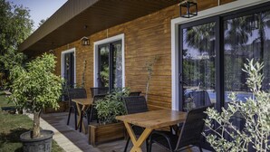 Puinen ulkoverhous, suuret ikkunat ja patio, jossa on ulkokalusteita.
