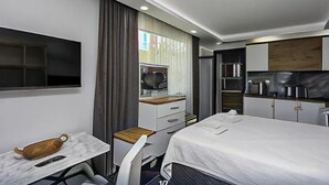 Pieni hotellihuone, jossa on sänky, työpöytä, tuoli, televisio, mikroaaltouuni ja pieni keittiönurkkaus.