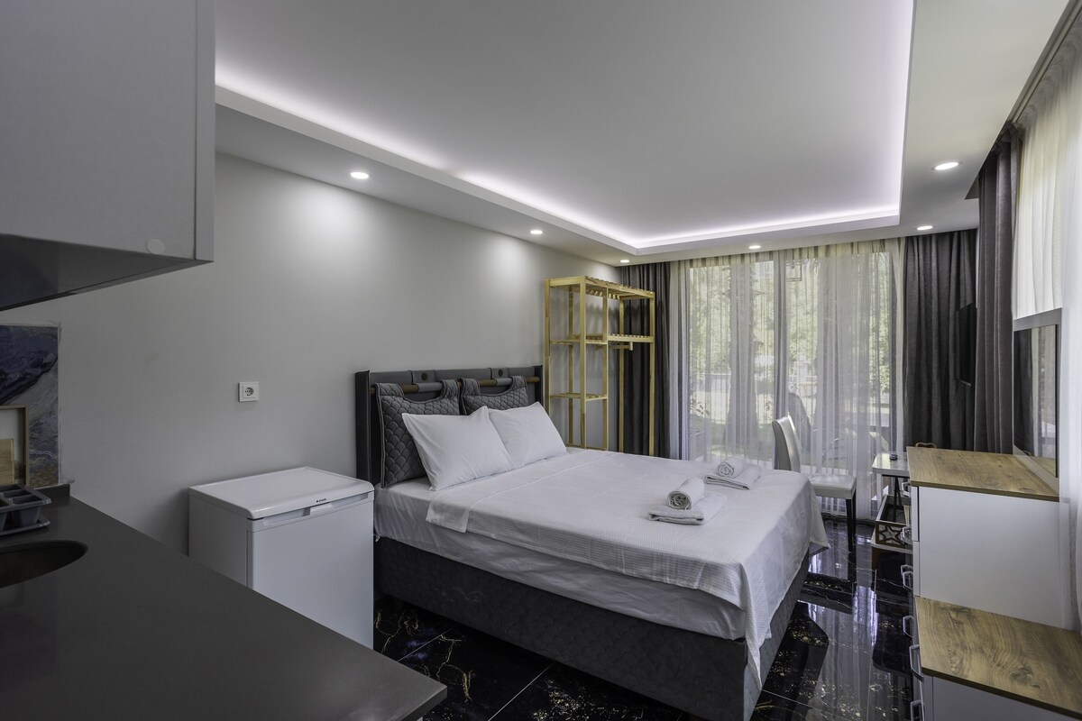 Quarto de hotel moderno com cama, mesa de cabeceira e uma pequena escrivaninha com cadeira.