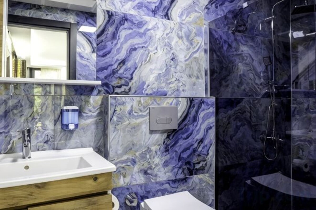 A bathroom with a marble backsplash, a sink, and a shower.