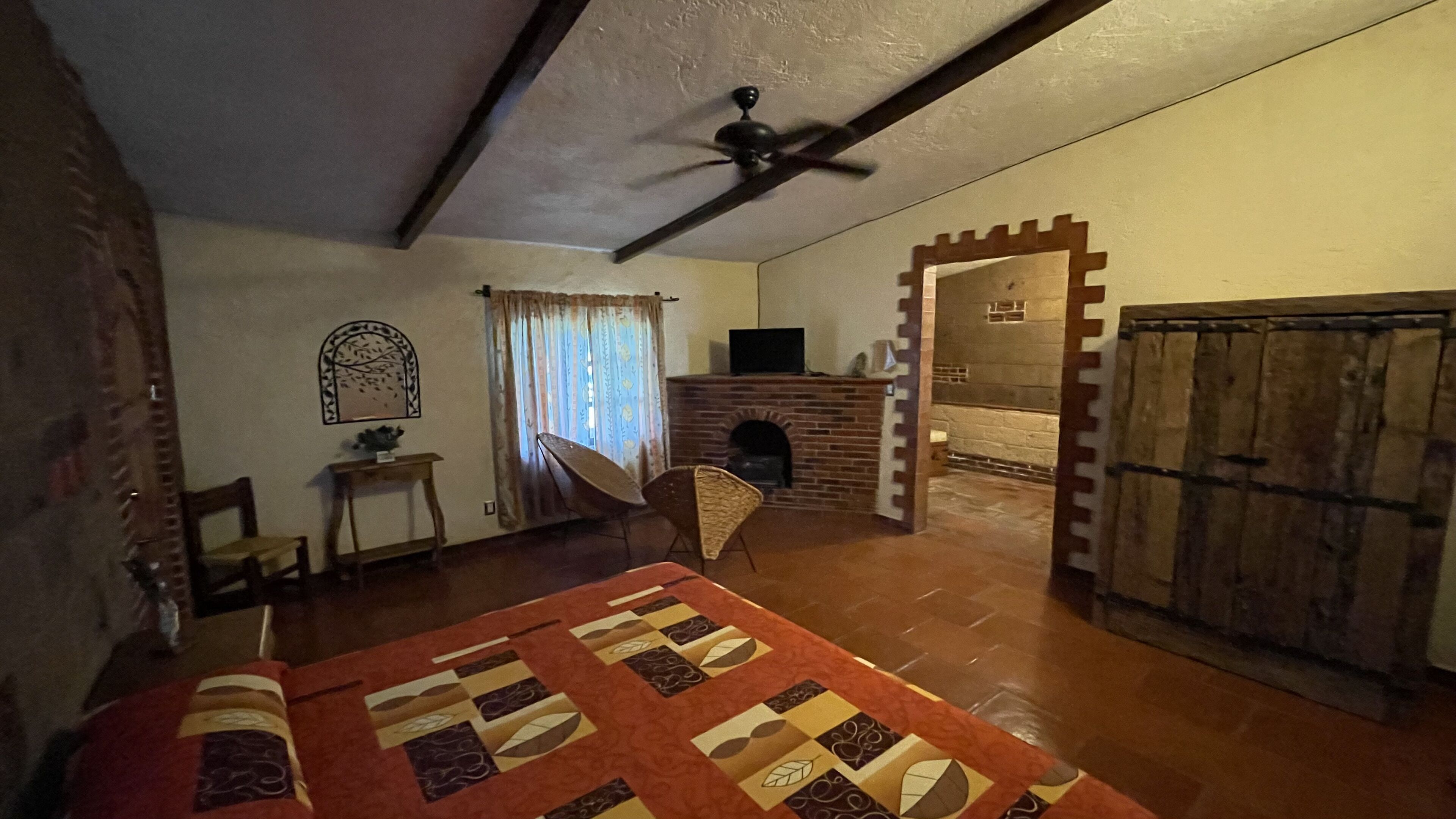 A cozy room with a fireplace, a ceiling fan, a bed with a patterned bedspread, and a rustic wooden door.