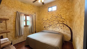 A bedroom with a bed, a window with curtains, a wall-mounted lamp, and a small window above the bed. - Casa Akbal (Malinalco)