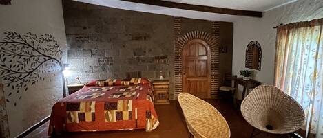 A bedroom with a bed, a chair, a wooden door, and a stone wall.