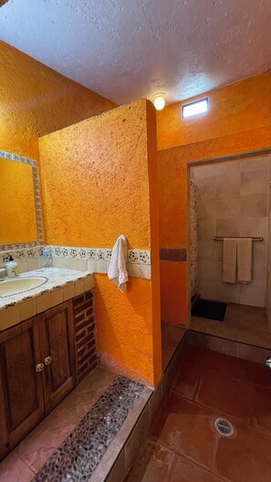 A bathroom with a tiled floor, a sink with a mirror, and a shower area. - Casa Akbal (Malinalco)