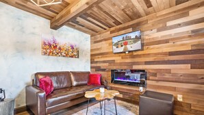 A cozy living room with a brown leather sofa, a wooden coffee table, and a flat-screen TV mounted on a wooden wall.