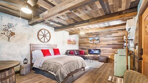 A cozy bedroom with a wooden ceiling, a bed with red and white bedding, a small table, and a vintage refrigerator.