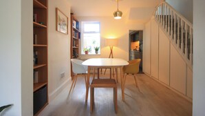 A dining area with a table and chairs, a bookshelf, a lamp, and a staircase. - Cosy Victorian house in south London with a sunny private garden. (LONDON)