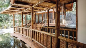 A bamboo structure with a wooden deck over water, leading to a building with large windows. - FLORBLANCA HOTEL  (Cóbano)