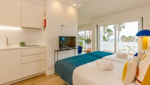 A hotel room with a bed, a TV, a desk, and a balcony with a view of palm trees.