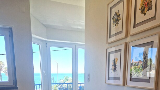 A living room with a beige sofa, a round table, and a view of the ocean through large windows. - NEW! ESTORIL SEAFRONT 1BEDROOM APARTMENT (Estoril)