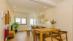 A spacious living area with a wooden dining table, chairs, a sofa, and a coffee table. There is a potted plant and a lamp on a side table. - NEW! ESTORIL SEAFRONT 1BEDROOM APARTMENT (Estoril)