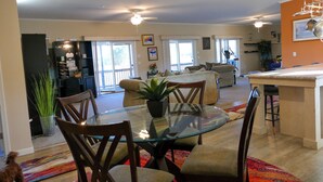 Un vaste espace de vie comprenant un coin repas avec une table en verre, des sièges confortables et une cuisine avec un bar.