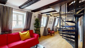 Une pièce avec un canapé rouge, un escalier et un coin repas.