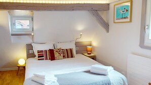 Une chambre à coucher avec un lit, des oreillers, une lampe de chevet, une fenêtre et un tableau encadré au mur.