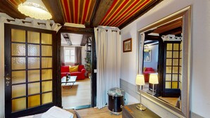 Une pièce avec un grand miroir, un canapé rouge, une petite table avec une lampe et une batterie.