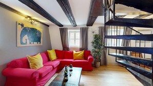 Un canapé rouge avec des coussins jaunes, une table basse en bois avec des bouteilles, un tableau représentant un éléphant bleu et un escalier avec une rampe en métal.