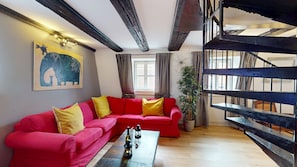 A red sofa with yellow cushions, a wooden coffee table with bottles, a painting of a blue elephant, and a staircase with a metal railing.