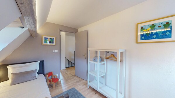 A bedroom with a bed, a chair, a wardrobe, and a door leading to another room.