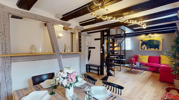 Un coin repas avec une table en bois dressée pour quatre personnes, un vase de fleurs et un escalier menant à une mezzanine.