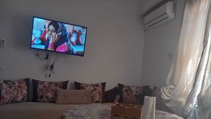 A living room with a sofa, a table with a floral tablecloth, a remote control, and a tissue box. - Marrakech Oasis Retreat - 4 Bed Apartment (Marrakech)