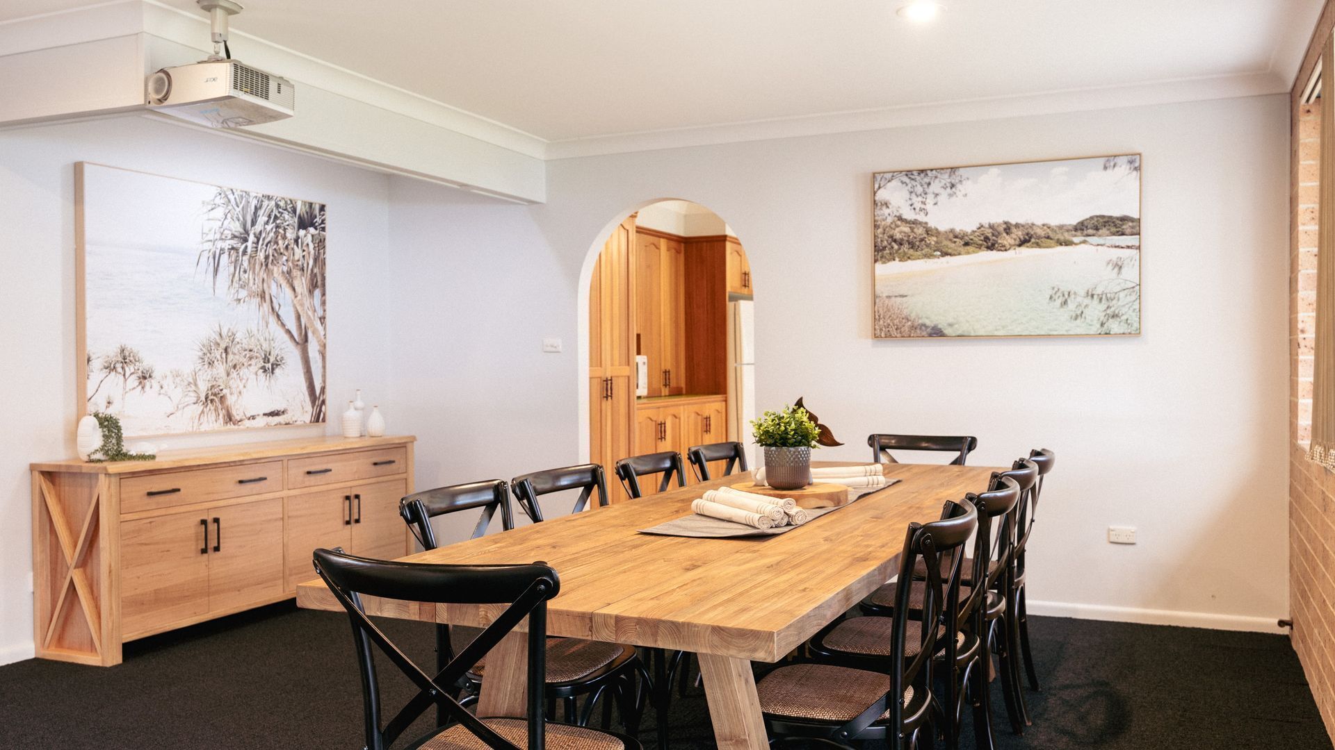 A dining area with a wooden table, black chairs, and a potted plant.