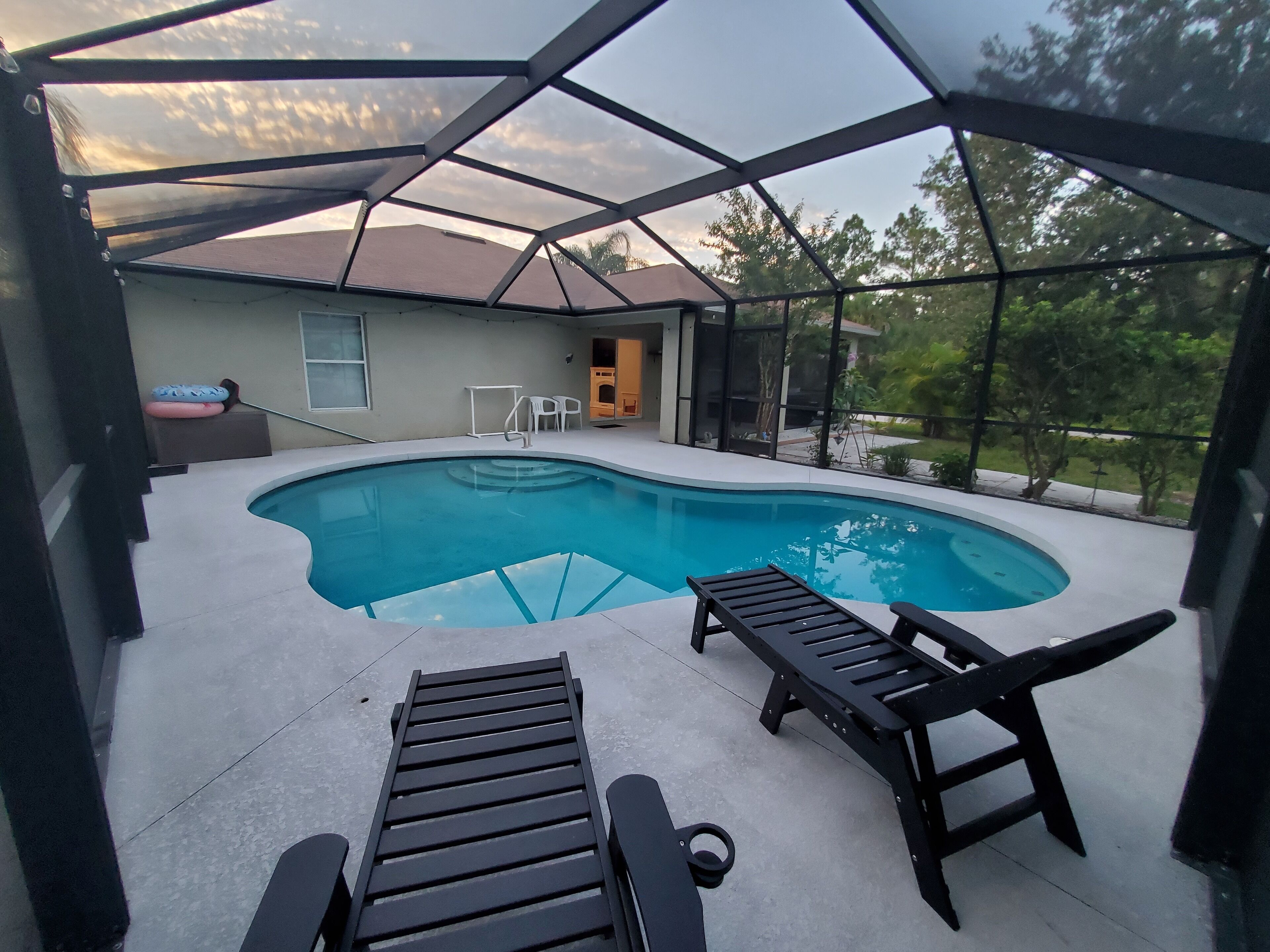 A swimming pool with two lounge chairs, a covered patio, and a view of the surrounding area.