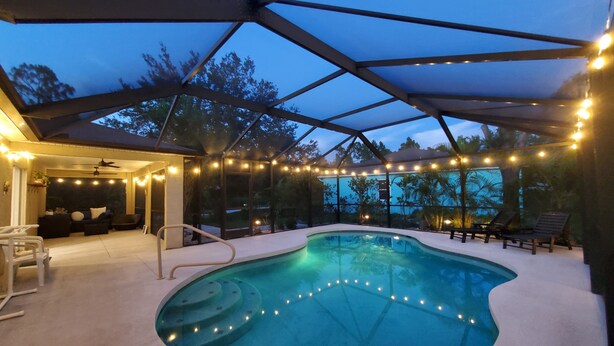 Piscina interior com design curvo, rodeada por um terraço coberto com luzes de corda.