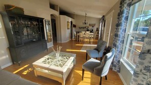 Uma sala de estar ampla com lareira, uma área de jantar e uma cozinha ao fundo.
