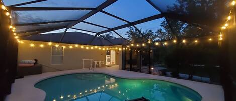 Una piscina con techo de vidrio, rodeada de luces colgantes, y un área de patio con sillones de descanso.
